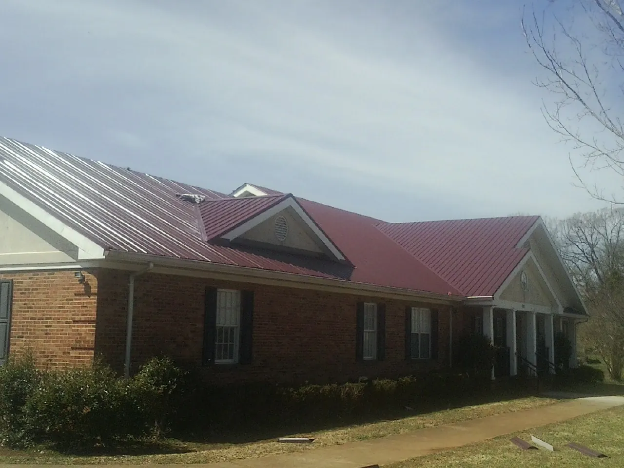 Red metal roof with gabled entries on a long brick building, from a Hail Damage Roof Repair job in Glen Saint Mary
