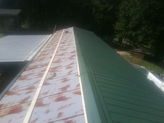 Old rusted panels beside newly installed green metal roofing — Wind Damage Roof Repair by Roofing Brothers in Glen Saint Mary
