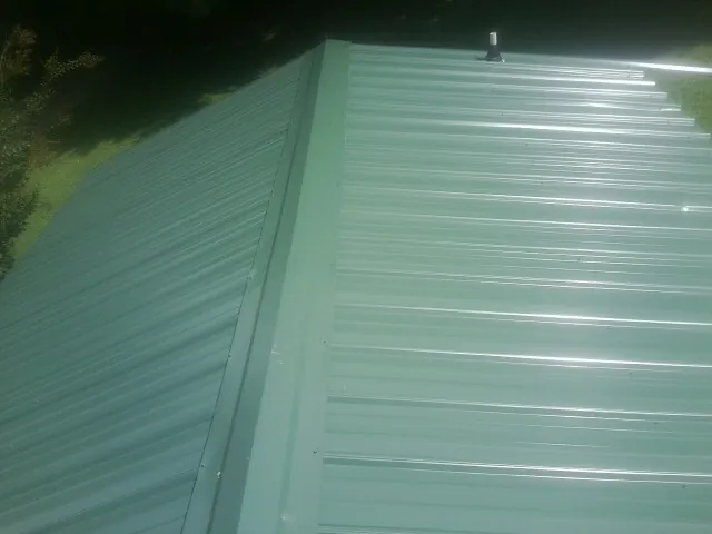 New green metal panels meeting at the ridge of a roof — Flat Roof Repair work by our crew in Glen Saint Mary
