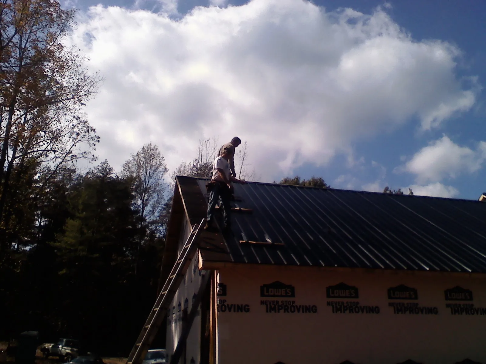 Roofer fastening dark metal panels high against a cloudy sky, from a Roof Inspection job in Glen Saint Mary