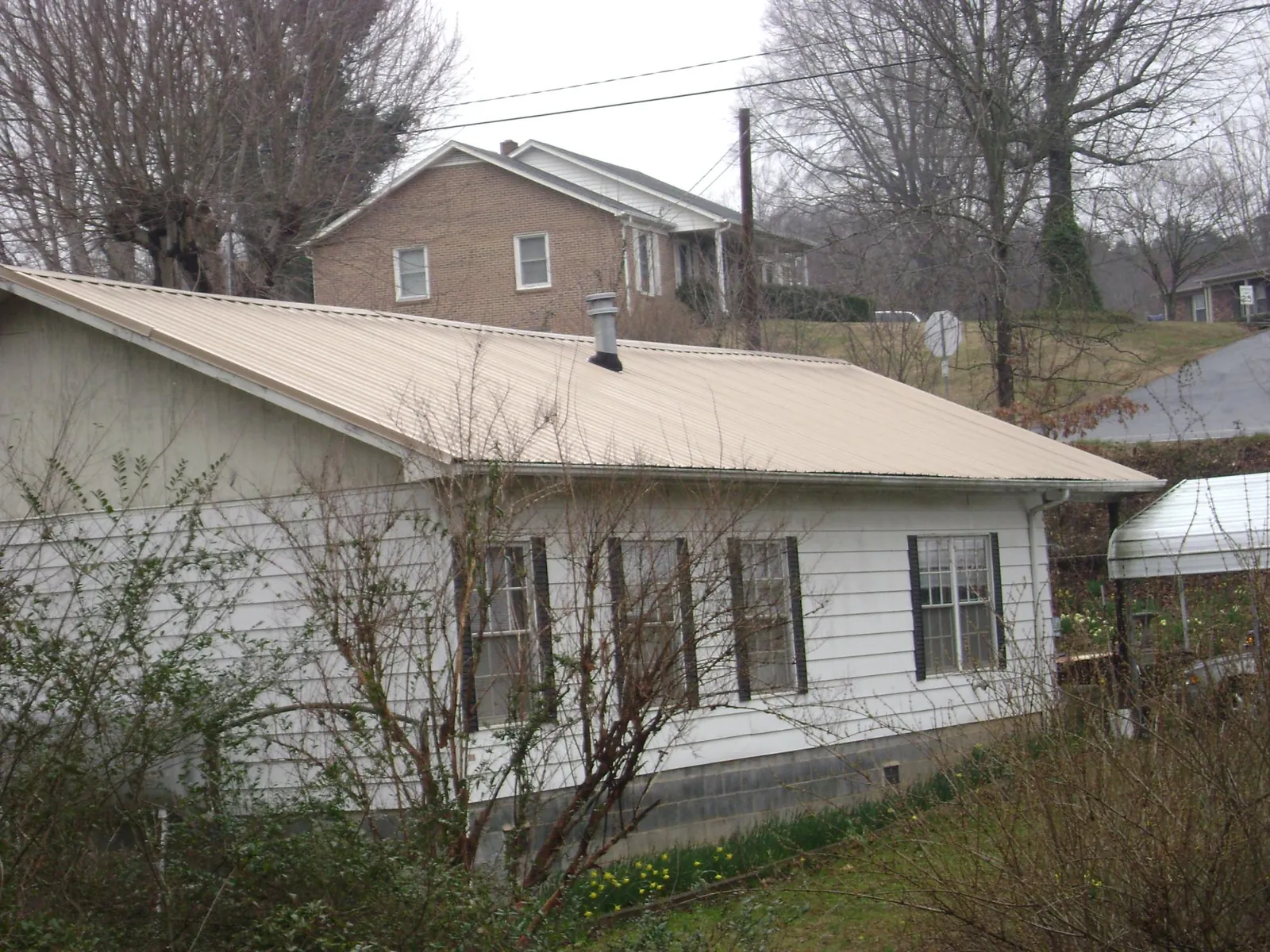 Tan metal roof on a white sided house set into a hillside — Commercial Roofing by Roofing Brothers in Glen Saint Mary
