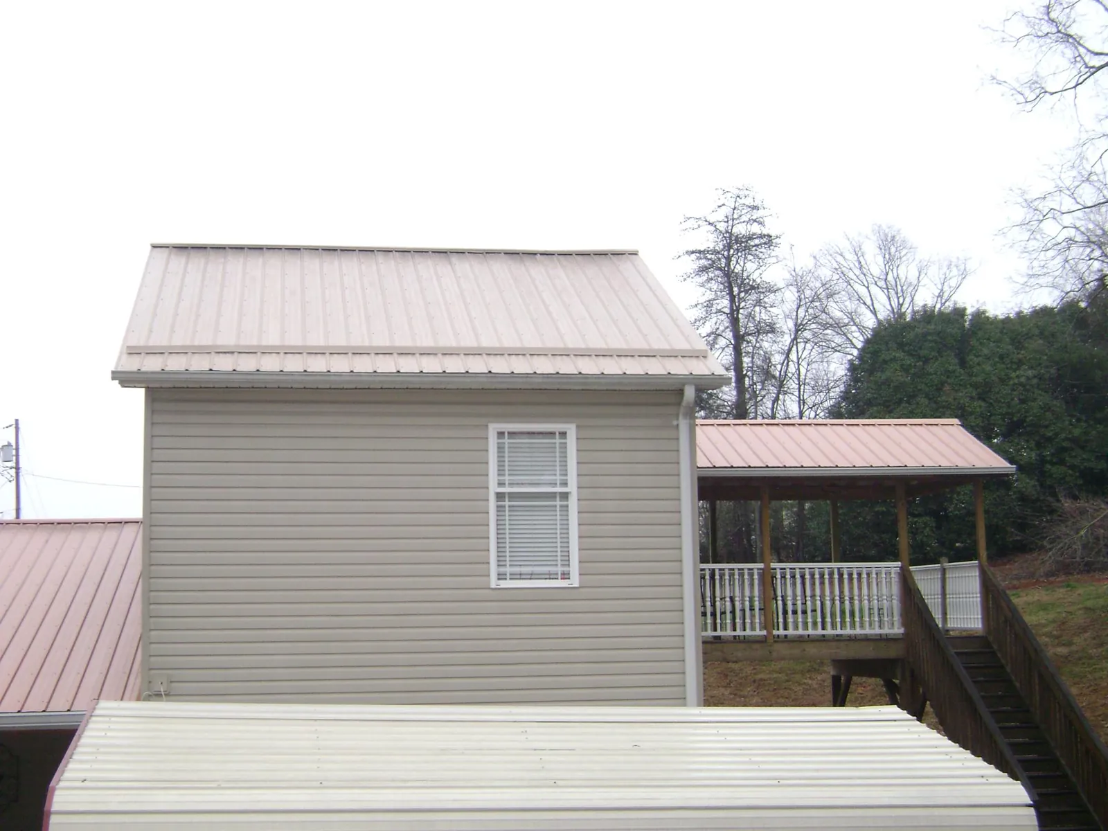 Tan metal roofs on a two story addition and attached porch, from a Roof Replacement job in Glen Saint Mary